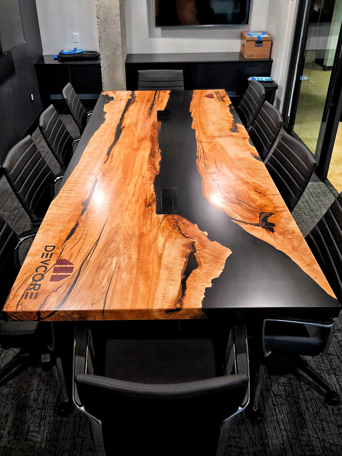 Maple conference table with black rivers of epoxy, central wireless charging ports, engraved company logo that read 'Devcore'