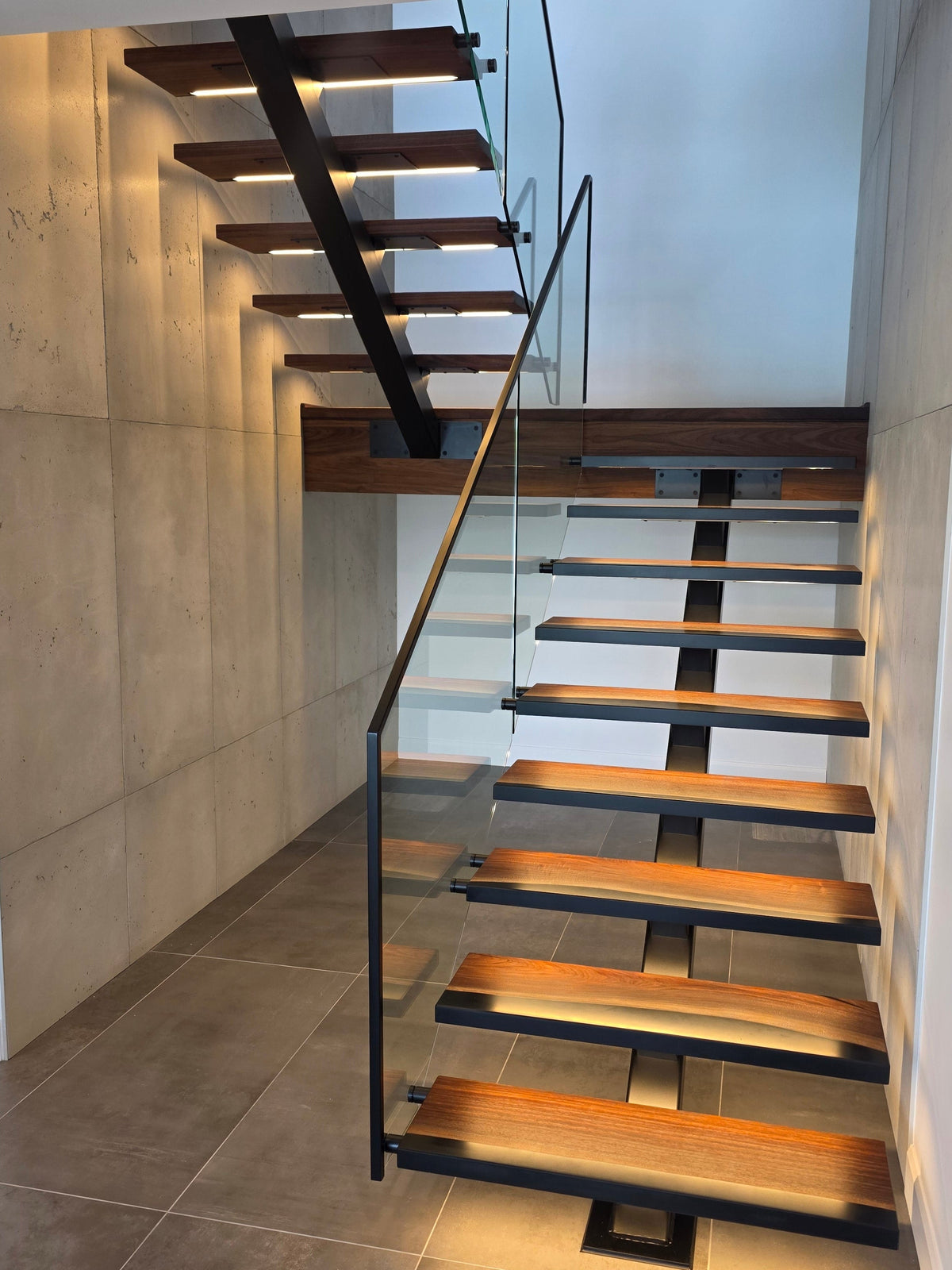 Modern staircase with glass railing and wooden walnut steps with custom LED lighting.