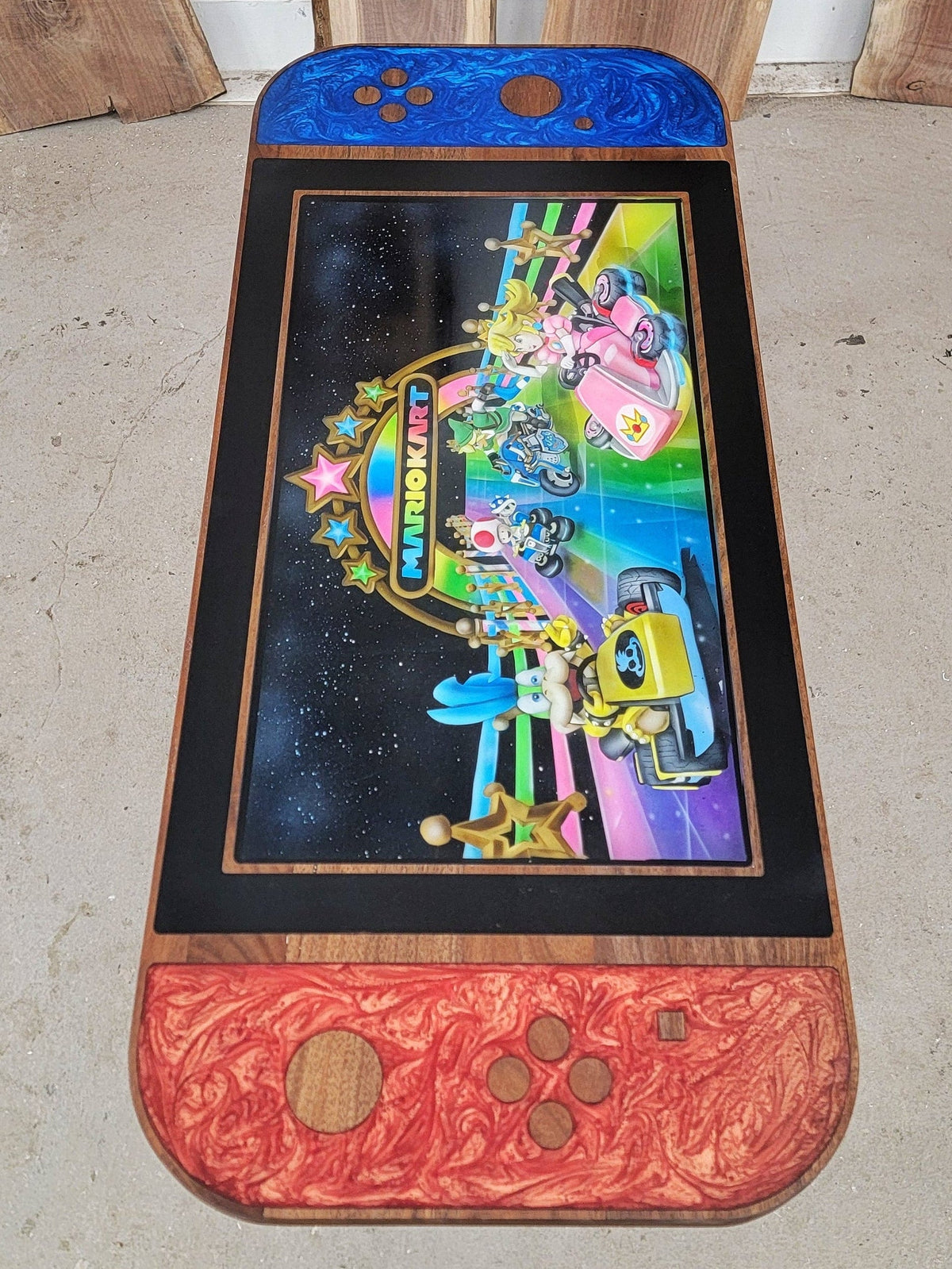Custom sized wood and epoxy coffee table. Shaped like a Nintendo Switch with red and blue epoxy on each controller; image is of a Mariokart race with Princess Peach, Koopa, Toad and Link driving on the Rainbow Road Stage built by Backyard Resin