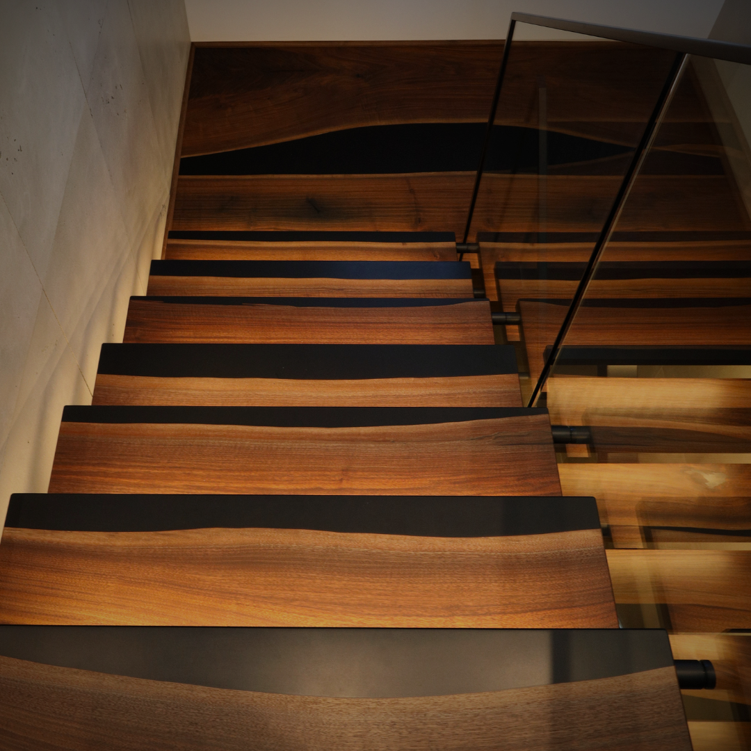 Custom walnut and black epoxy staircase with walnut and black epoxy landing featuring integrated LED lighting under each step built by Backyard Resin.